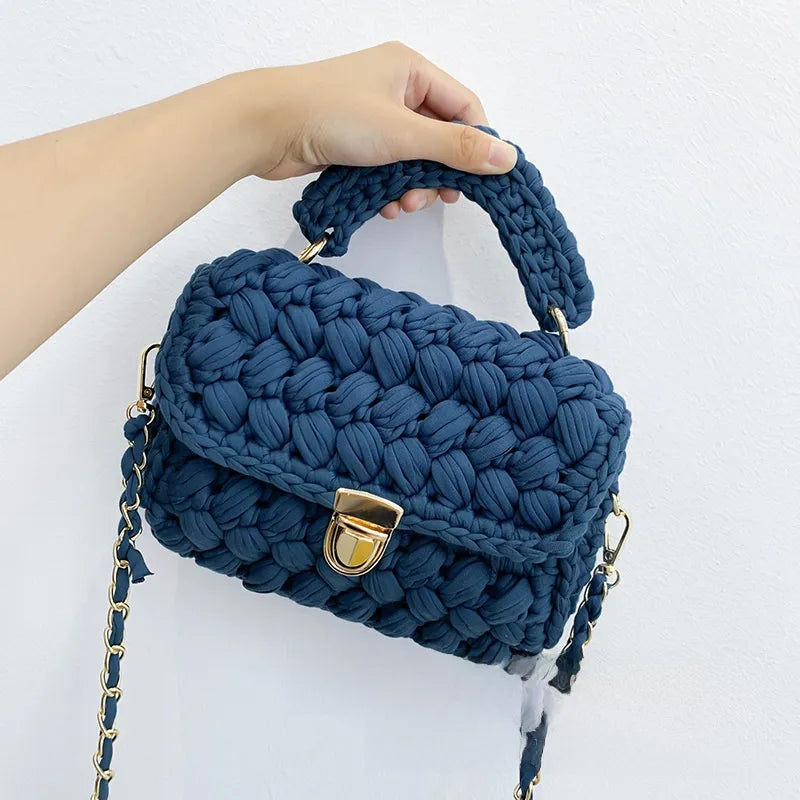 Blue woven handbag with a gold clasp held by a hand on a white background